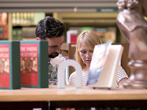 Two people looking at something behind a book shelf