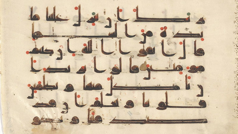 Section of a manuscript leaf covered with thick black Arabic script accented by gold and red markings