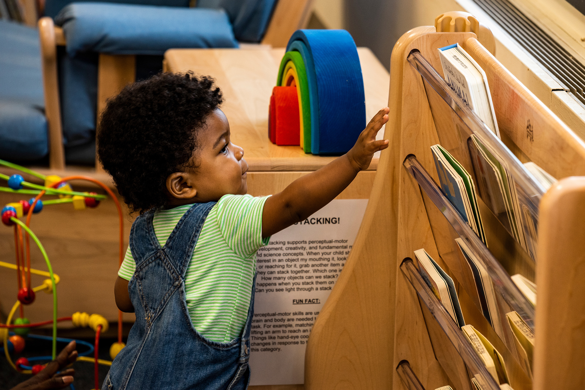 A child reaches for a board book on a library shelf. Photo by Chris Baker Evens.