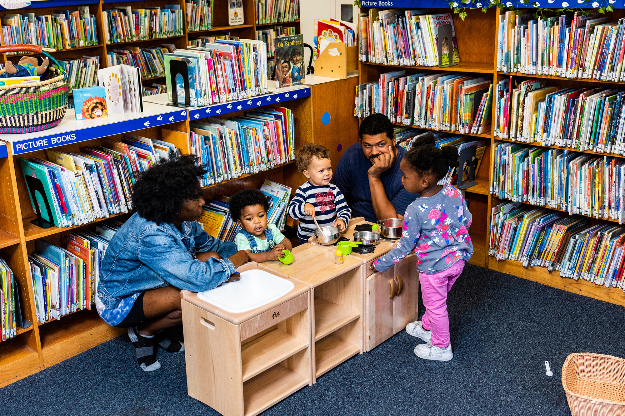 Two adults and three children gather around a play kitchen in the library. Photo by Chris Baker Evens.