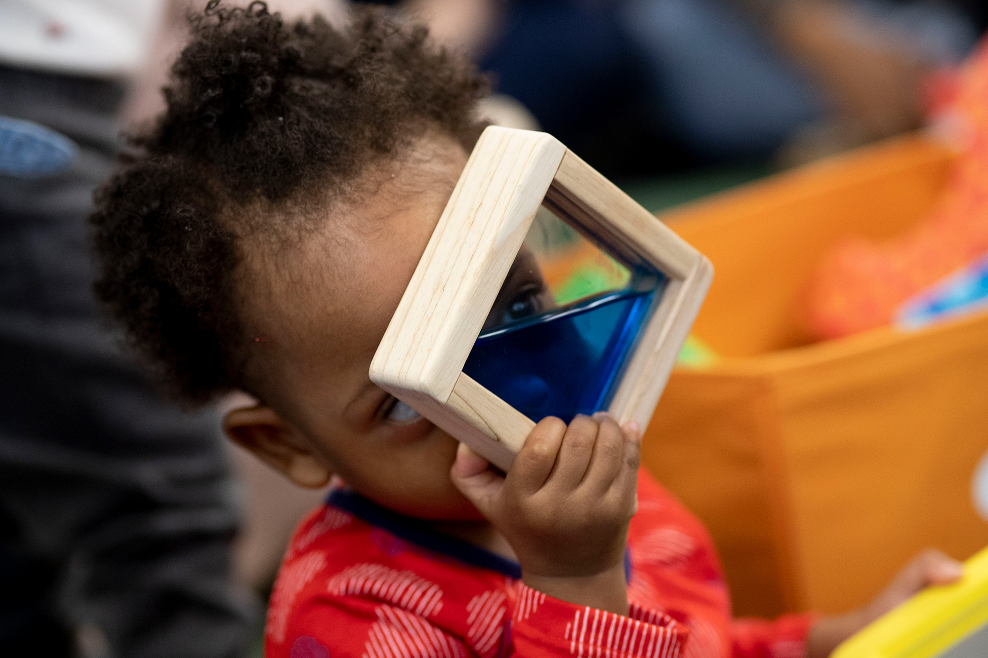 A child peers through a blue color viewer toy. Photo by Ryan Brandenberg.