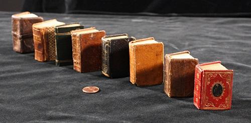 Miniature books lined up with a penny for scale