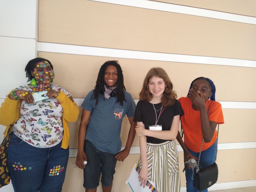 Four teens smiling, one covered in stickers and one laughing