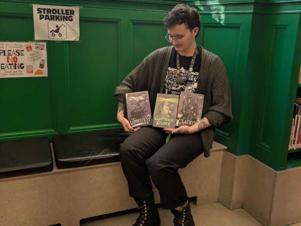 Person with glasses sitting holding 3 children's books