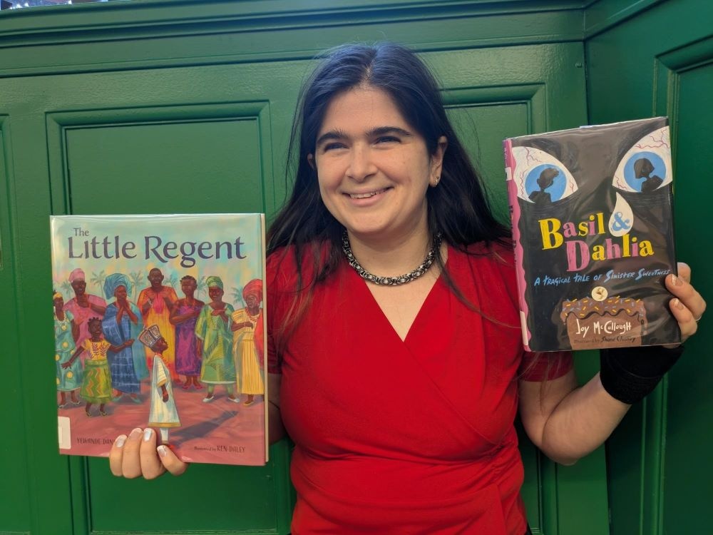 Woman with long hair smiling and holding up 2 children's books