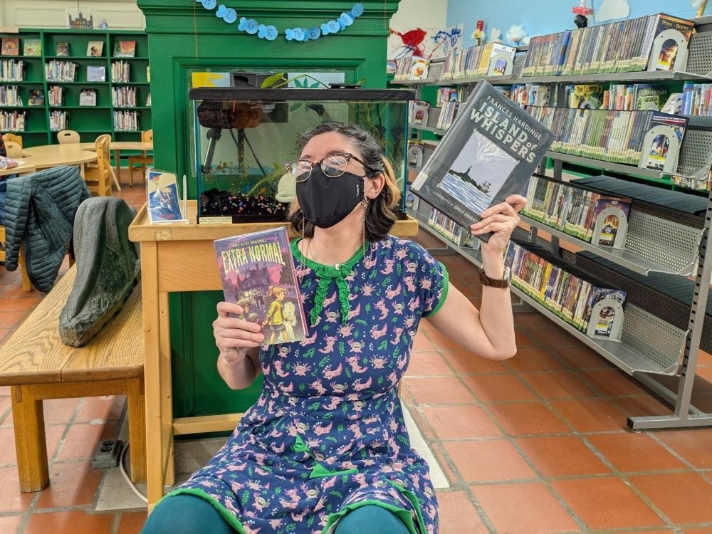 person wearing glasses and face mask holding up 2 children's books