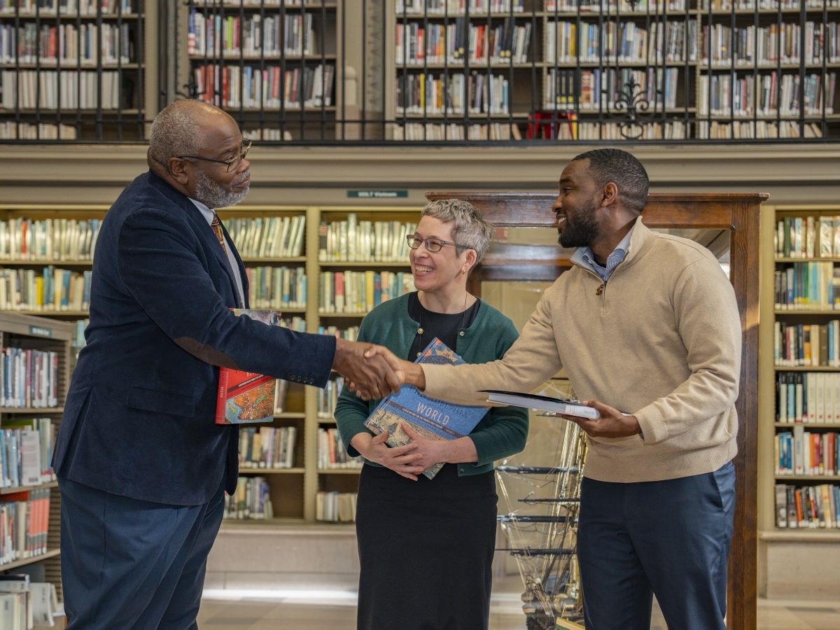 Free Library President Kelly Richards shaking hands with two people holding books in library setting