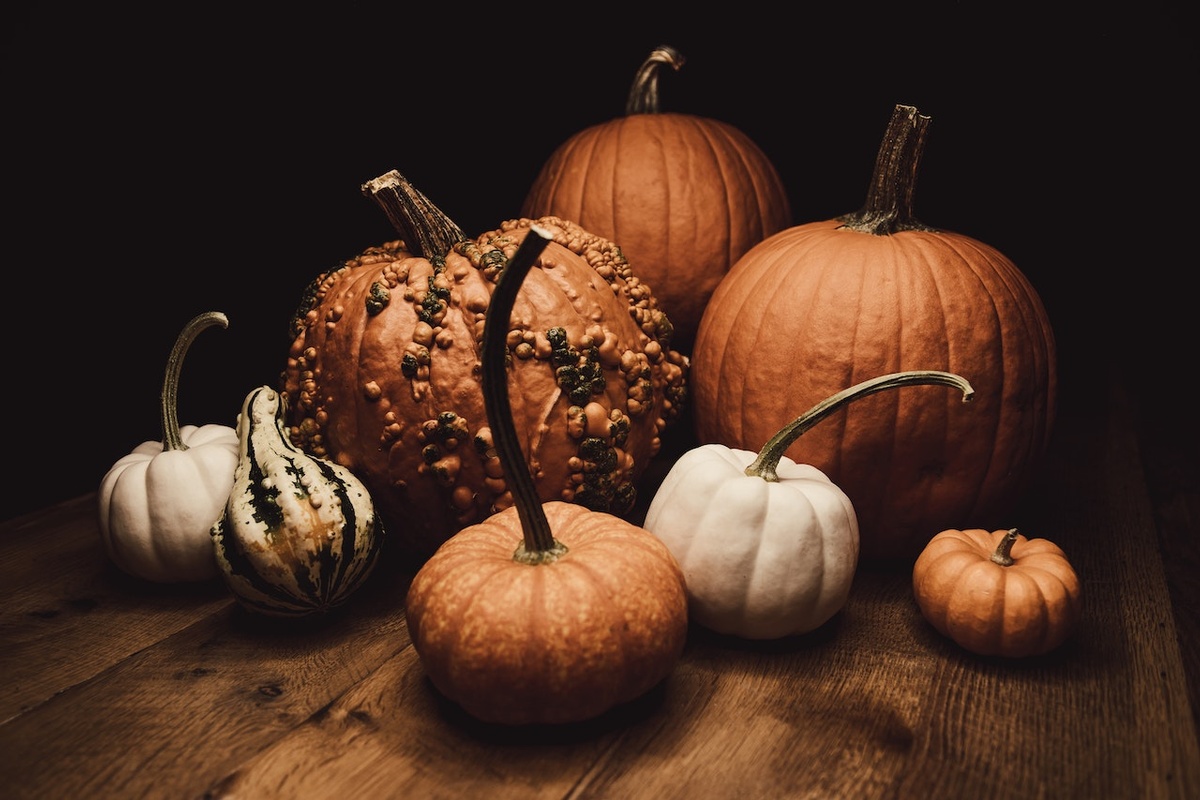 A collection of orange pumpkins and green and white gourds rest on a dark wooden table.