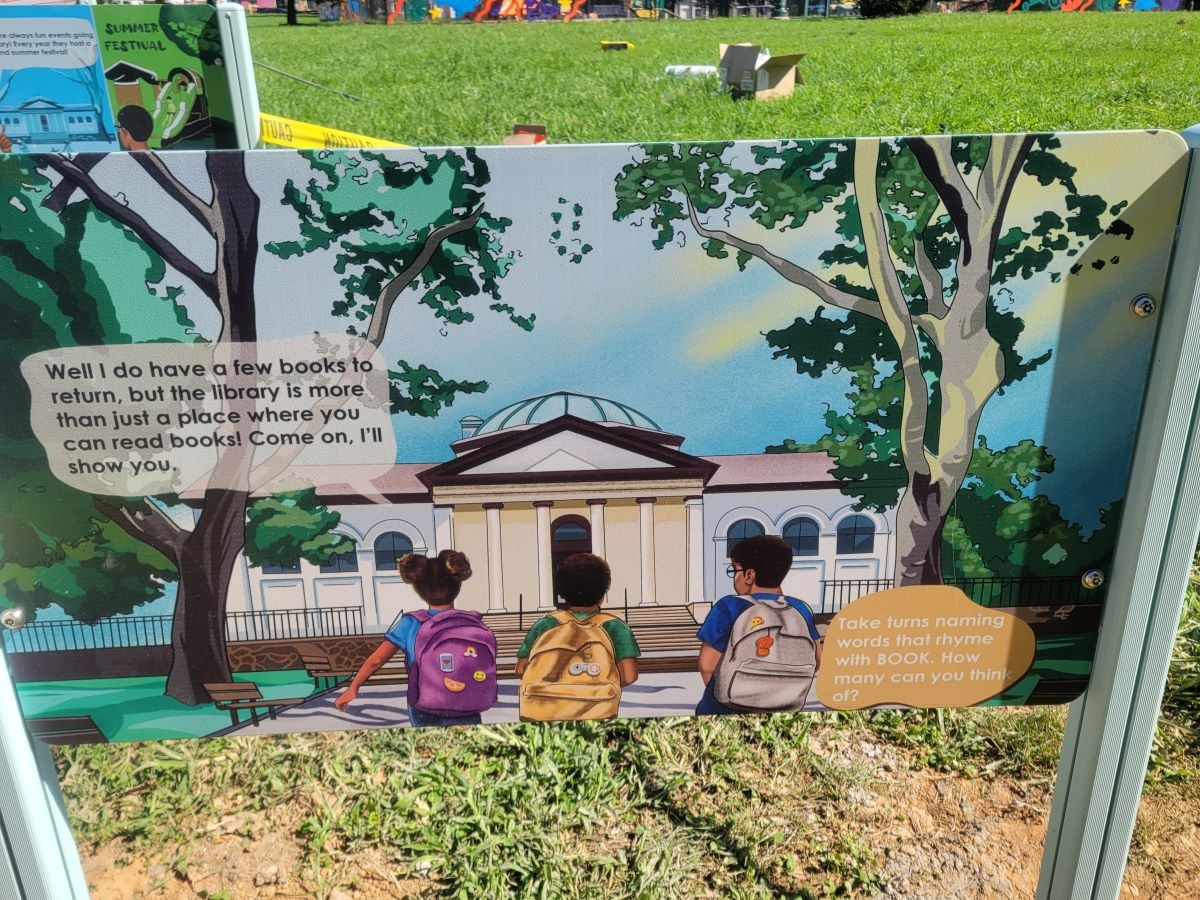 children in park facing the library discussing returning their books