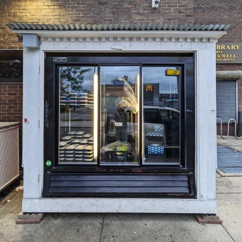 Large glass-doored outdoor refrigerator on the sidewalk in front of brick library building