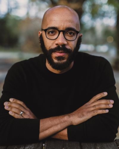 headshot of man with glasses and arms crossed sitting at outdoor table