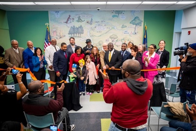 diverse group of people smiling holding cut ribbon in front of mural
