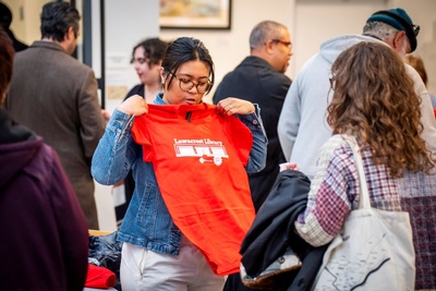 bespectacled woman holding up shirt with illustration of Lawncrest Library on it