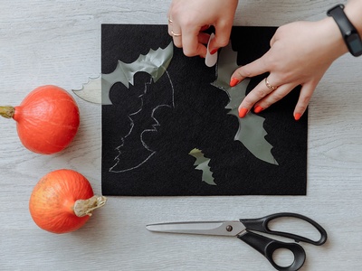 a set of hands cutting out a bat shape from black construction paper